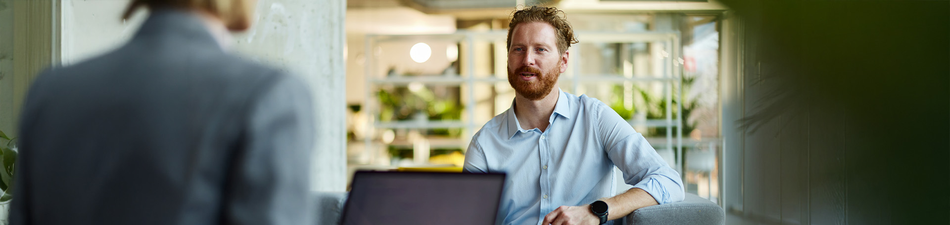 Eine Person spricht in einem Bürogespräch mit einer weiteren Person, ein Laptop steht auf dem Tisch.