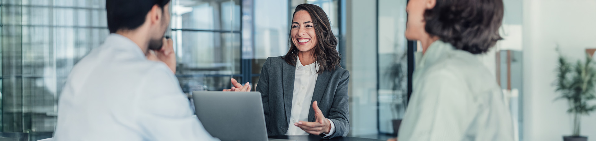 Gesprächssituation mit drei Personen in einem modernen Büro, eine Person erklärt etwas mit Unterstützung eines Laptops.